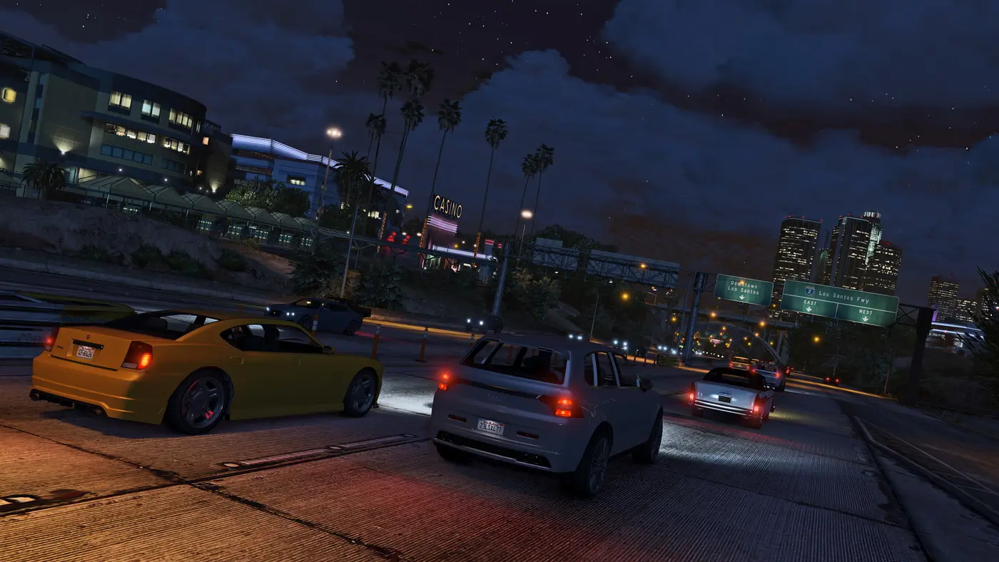 Los Santos at night in GTA 5, an urban freeway, a casino sign and the downtown skyscrapers lit up in the distance under a starry sky