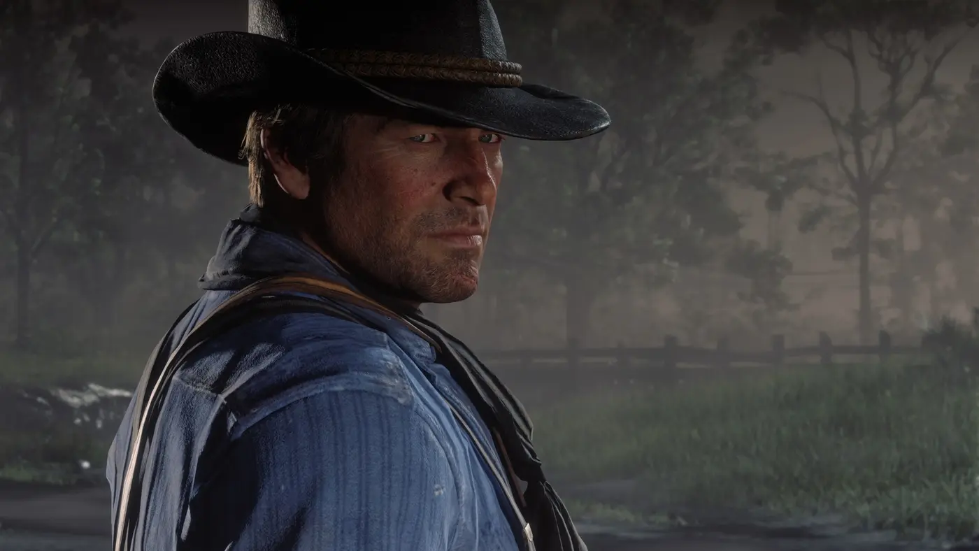 Official Red Dead Redemption 2 screenshot: a close-up of Arthur Morgan's face under his black hat, stubble, weathered and detailed skin, against a misty forest