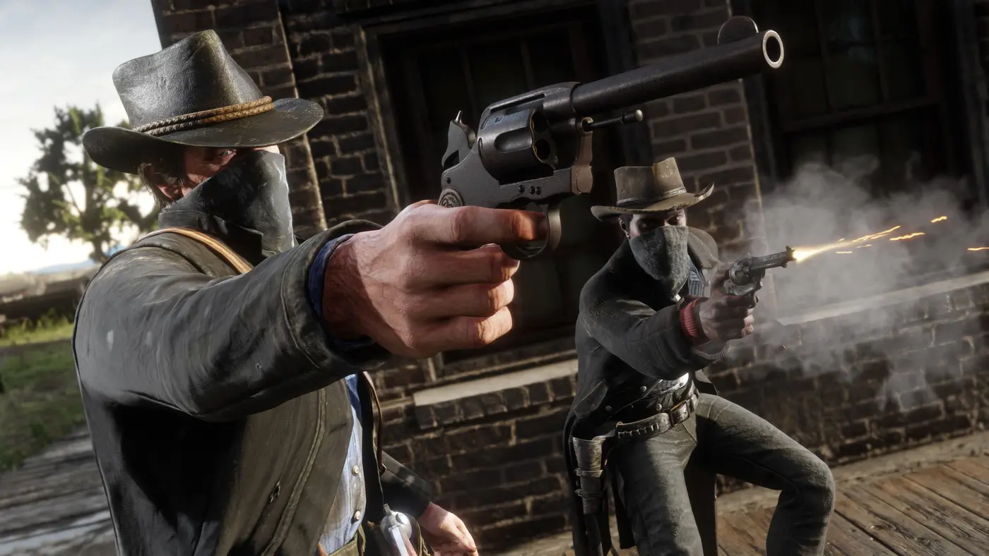 Official Red Dead Redemption 2 screenshot: two masked outlaws fire revolvers toward the camera, sparks and smoke at the muzzle, in front of a brick facade