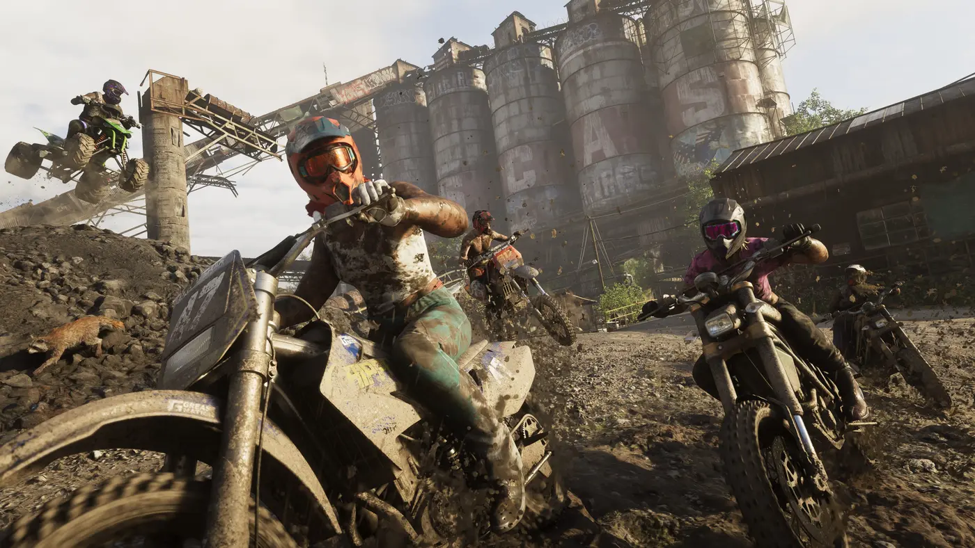 Several mud-splattered dirt bike riders launching in front of large tagged industrial silos in GTA 6